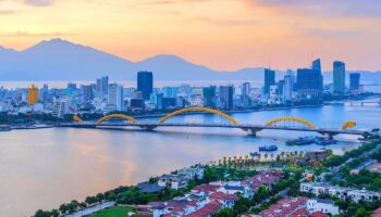 Vue panoramique de Da Nang au coucher du soleil avec le pont du Dragon illuminé et les montagnes en arrière-plan
